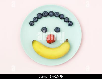 Beeren und Banane auf blauem Teller in Form eines glücklichen Gesichts angeordnet Stockfoto