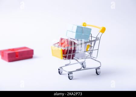 Miniaturwagen mit Geschenken auf weißem Hintergrund. Shopping-Konzept für den Urlaub. Neujahr, Weihnachten, Geburtstag. Selektiver Fokus, Nahaufnahme. Stockfoto