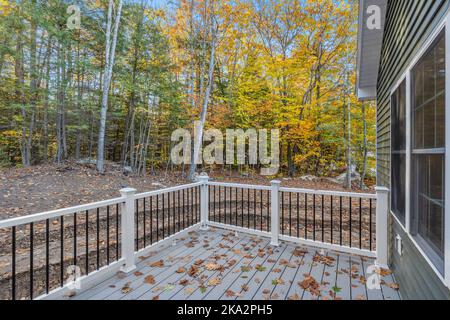 Eine kleine Herbstterrasse mit Blick auf ein neu erbautes Haus, umgeben von Bäumen und Blättern Stockfoto