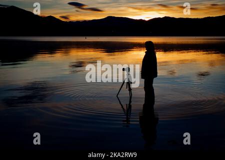 Eine Silhouette eines Fotografen am Wanaka-See bei Sonnenaufgang in Central Otago, Neuseeland. Stockfoto