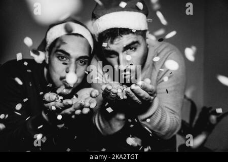 Happy Gay Männer Paar bläst Konfetti und trägt Weihnachtsmann Hüte während Heiligabend - Weiche Fokus auf die Hände - Schwarz-Weiß-Schnitt Stockfoto
