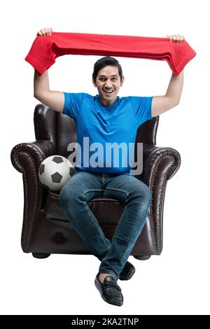 Asiatischer Mann mit dem Ball hält Schal sitzen auf der Couch mit einem aufgeregt Ausdruck isoliert auf weißem Hintergrund Stockfoto