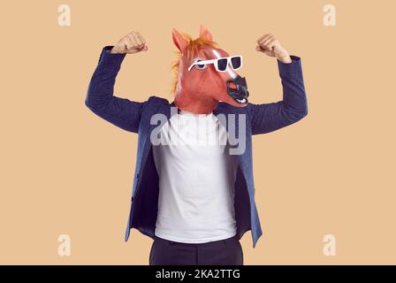 Mann im Anzug, lustige Pferdemaske und Sonnenbrille zeigt seine Kraft und beugt seine Arme Stockfoto