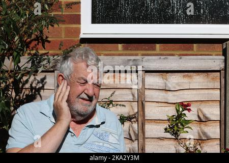 Älterer Mann mit Ohrenschmerzen. In großen Schmerzen und das Ohr haltend. Ohrinfektion. Stockfoto