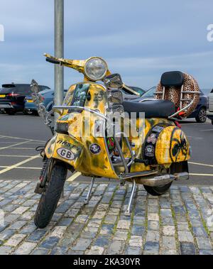 Ein Vespa Scooter mit seinem maßgefertigten Stil und seiner Lackierung parkte am Meer in Saltburn, North Yorkshire. Stockfoto