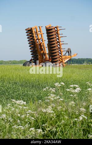 Eine große Scheibenegge, die von Traktoren zum Pflügen von Feldern gegen den Himmel geschleppt wird Stockfoto