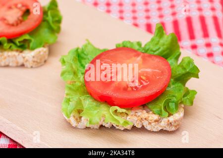 Reiskuchen-Sandwiches mit Tomaten und Salat auf Holzbrett. Einfaches Frühstück. Diät-Essen. Schnelle und gesunde Sandwiches. Knäckebrot mit leckerer Füllung. Gesunder Ernährungs-Snack Stockfoto