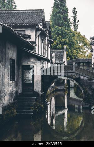 Eine vertikale Aufnahme einer gewölbten Steinbrücke über einen Kanal mit Reflexion auf Wasser in Wuzhen, China Stockfoto
