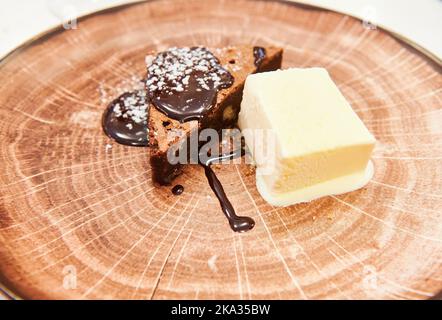 Schokoladen-Brownie-Dessert mit Vanilleeis auf imitiertem Holzteller Stockfoto