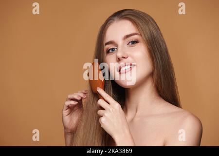 Frau kämmt ihre langen natürlichen Haare mit Holzpinsel Stockfoto