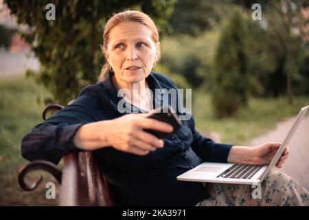 Ältere Geschäftsfrau mit Laptop und Smartphone im Park Stockfoto