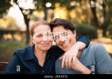 Glückliche reife Mutter umarmt lächelnden erwachsenen Sohn im Park im Sommer Stockfoto