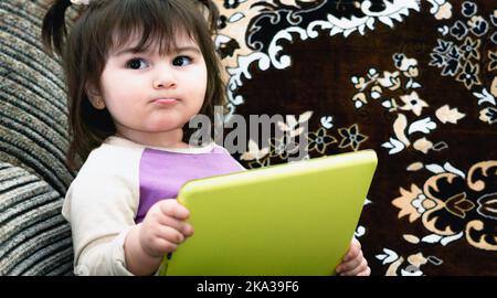 Ein entzückendes kleines Baby aus nächster Nähe, das mit einem Tablet Musik über Kopfhörer hören kann Stockfoto