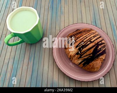 Eine leckere Frühstückskombo mit eisgekühltem, geschüttelten Matcha Latte und einem Schokoladencroissant auf einem verzweifelten blauen Holztisch Stockfoto