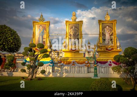 Riesige Porträts des thailändischen Königs und seiner Familie zieren ein Denkmal am Wat Arun oder am Tempel der Morgenröte am Ufer des Chao Phraya Flusses in Bangkok, Stockfoto