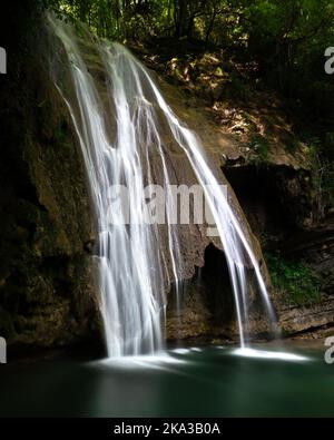 Eine schöne Aussicht auf fließenden Wasserfall von Felsen im Hintergrund von Bäumen Stockfoto