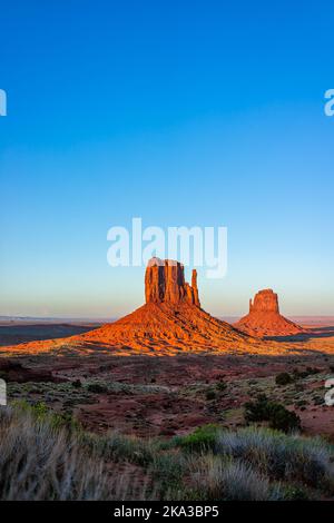 Monument Valley berühmte Buttes vertikale Ansicht bei bunten roten Sonnenuntergang in Arizona mit orangen Felsformationen und blauen Himmel mit Ost-und West-Fäustlinge Sha Stockfoto