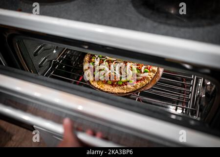 Hand öffnen Ofentür Überprüfung hausgemachte Pizza Kochen Backen mit Tomatensauce, Belag grünen Paprika Zwiebeln gehackt mit gemahlener Wurst crumbl Stockfoto