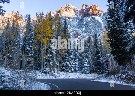 Maroon Bells Creek Leere Straße in Aspen, Colorado die Rocky Mountains sind nach dem Schneefall im Spätherbst mit Sonnenlicht auf der Spitze und dunklem Waldgelb bedeckt Stockfoto