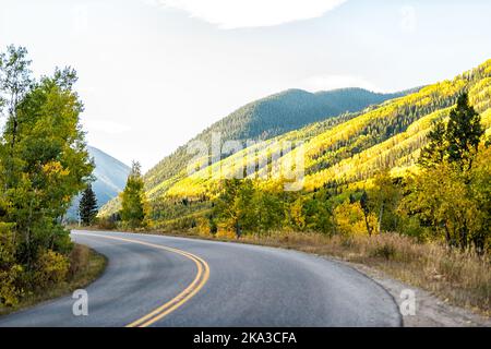 Colorado Rocky Mountains mit Castle Creek malerische gepflasterte Straße, die sich bei Sonnenuntergang schlängelt, mit farbenprächtigem, gelb-orangefarbenem Laub im Herbst auf Bäume fällt Stockfoto