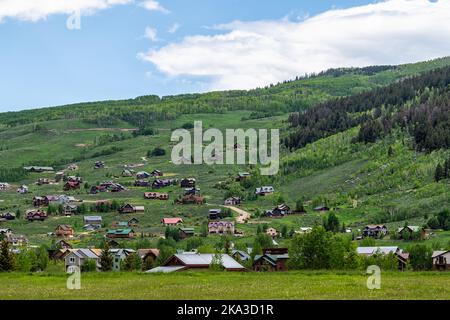 Mount Crested Butte Dorf Stadthäuser im Sommer mit vielen hölzernen Unterkünften Gebäude auf Hügel mit grünen üppigen Farben Gras Stockfoto