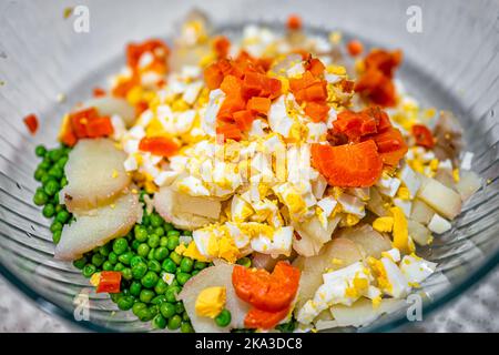 Makro Nahaufnahme der Vorbereitung Vorbereitung traditionelle ukrainische oder russische Salat Olivie olivier mit geschnittenen Kartoffeln Karotten Erbsen, Ei in Rührschüssel Stockfoto