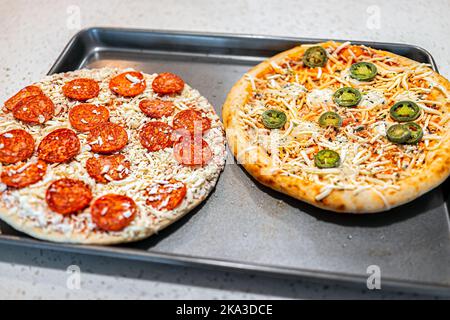 Makro-Nahaufnahme von ungekochten rohen nehmen und backen gefrorenen Pepperoni zerfetzten Mozzarella-Käse und Jalapeno Pizzakuchen auf dem Tablett bereit zum Backen Kochen auf Kit Stockfoto