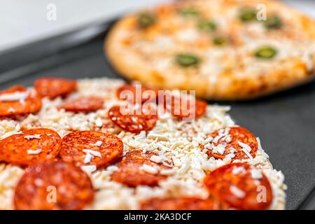 Makro-Nahaufnahme von ungekochten rohen nehmen und backen gefrorenen Pepperoni zerfetzten Mozzarella-Käse und Jalapeno Pizzakuchen auf dem Tablett bereit zum Backen Kochen auf Kit Stockfoto