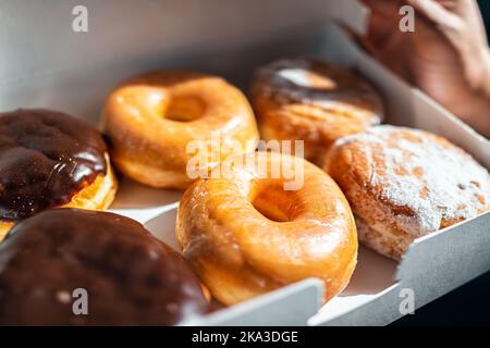 Mann hält ein halbes Dutzend Donuts Donuts in Karton-Container-Box, glasierte frittierte Dessertgebäck von Boston-Creme, Schokolade Füllung Stockfoto