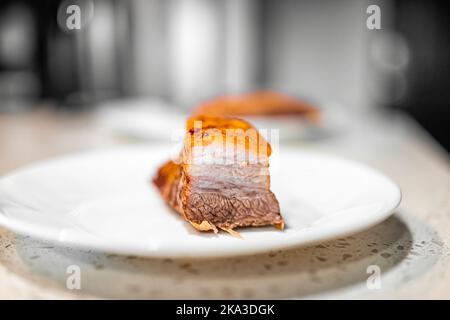 Makro-Nahaufnahme von geschnittenem frischem Grill gekochtem gebackenem Schweinefleischbauch Bauchfett Speck Fleisch mit knuspriger knuspriger Haut, nahrhaftes Essen gegen weißen Teller bei k isoliert Stockfoto