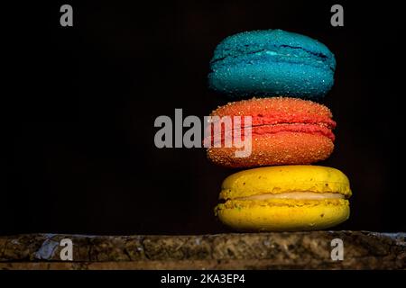 Bunte französische Makronen mit verschiedenen Füllungen auf Holztisch in dunklem Hintergrund platziert Stockfoto