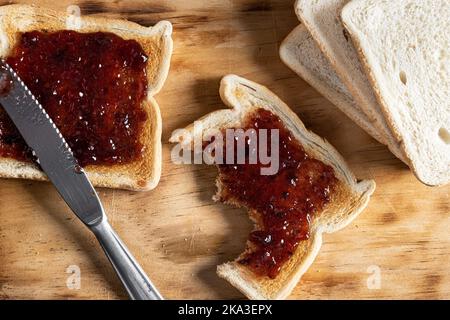 Blick von oben auf appetitliche knusprige Toasts mit Kirschmarmelade auf einem Holzbrett Stockfoto