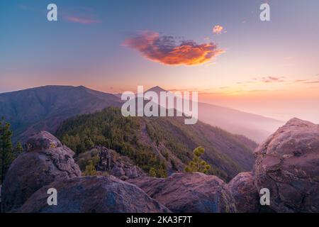 Drohnenansicht des malerischen bergigen Tals mit grünen Nadelbäumen unter bunt bewölktem Sonnenuntergang Stockfoto