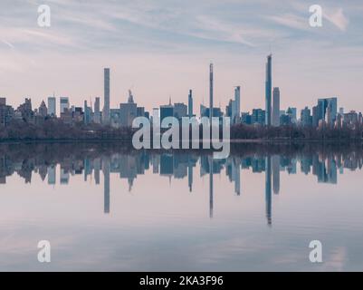 Ruhiges Wasser mit sauberem Teich, das Wolkenkratzer und bewölkten Sonnenuntergangshimmel reflektiert, im Central Park in New York, USA Stockfoto