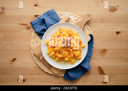 Blick von oben auf köstlichen frischen, gesunden Salat mit Kürbissen, roten Paprika und Kirschtomaten, serviert auf Tellern auf einem Holztisch in der Küche Stockfoto