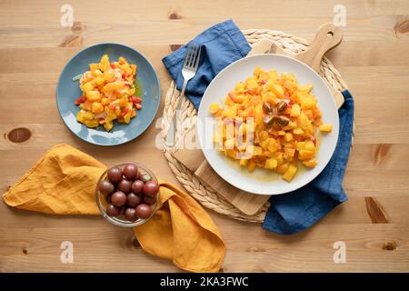 Blick von oben auf köstlichen frischen, gesunden Salat mit Kürbissen, roten Paprika und Kirschtomaten, serviert auf Tellern auf einem Holztisch in der Küche Stockfoto
