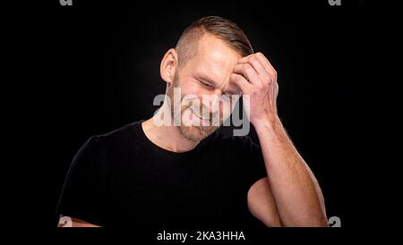 Ein Mann lächelt in einem seltsamen Setting vor dunklem Hintergrund. Stockfoto