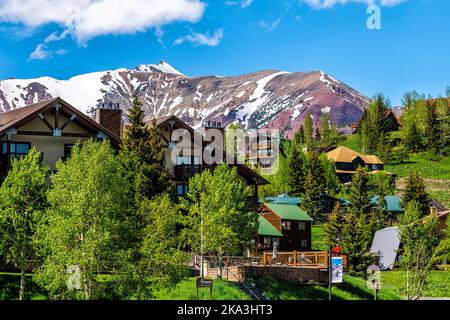 Mount Crested Butte, USA - 20. Juni 2019: Schneebedeckter Berg im Sommer mit grünen Hügeln und Hanghäusern Ponderosa Wohnanlagen Gebäudekomplex Stockfoto