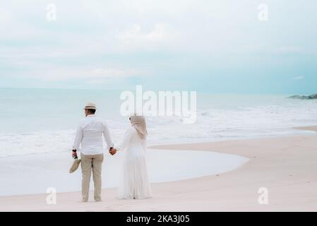 Ein Paar genießt die Strandwellen zusammen mit den Händen und steht am Sandstrand Stockfoto