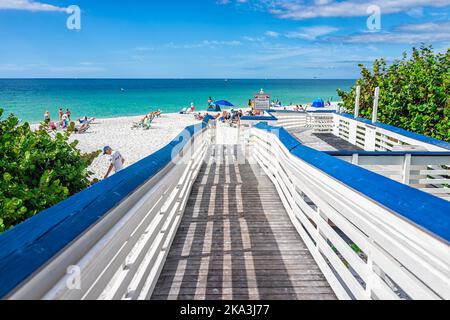 Naples, USA - 4. Dezember 2021: Rampe am Clam Pass Park Strand von Collier County, Florida mit Menschen Sonnenbaden unter Sonnenschirmen auf Stühlen mit Beautifu Stockfoto