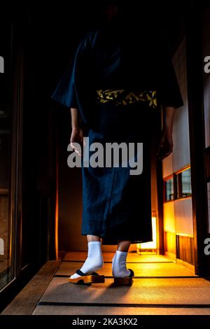 Nicht erkennbarer Mann im japanischen Kimono, der nachts mit geta-Socken und Tabi-Schuhen durch Shoji-Schiebetüren aus Papier und Tatami-Matten-Vertikalansicht in tra läuft Stockfoto