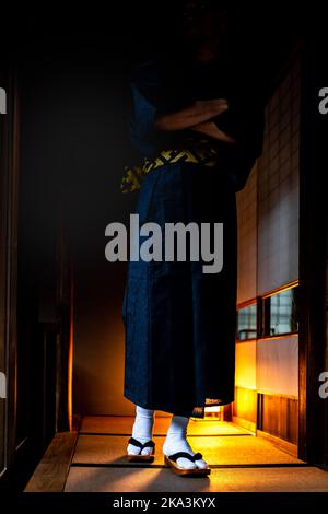 Mann im japanischen Kimono, der mit geta-Socken an den Füßen und Tabi-Schuhen durch Shoji-Schiebetüren aus Papier und Tatami-Matte in der vertikalen Ansicht im traditionellen Haus r Stockfoto