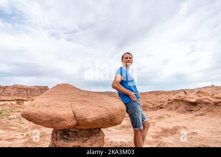 Mann Wanderer durch einzigartige Hoodoo Sandstein Felsformationen Wüstenlandschaft im Goblin Valley State Park in Utah auf dem Weg mit Wolken am Himmel Stockfoto