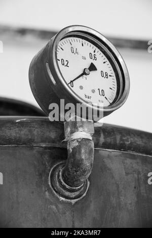 Eine vertikale Graustufenaufnahme eines alten Druckmessers eines Tanks Stockfoto