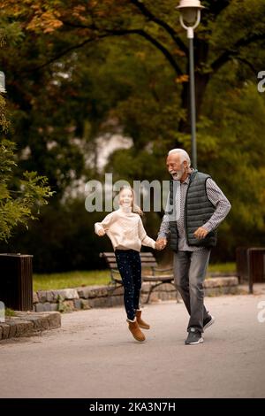 Der gutaussehende Großvater verbringt am Herbsttag Zeit mit seiner Enkelin im Park Stockfoto