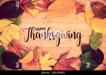 Happy Thanksgiving geschrieben in einem Rahmen von bunten Herbstblättern, Holzhintergrund Stockfoto