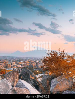 Ein vertikaler atemberaubender Blick auf das Stadtbild von Jerewan hinter den Felsen mit der Silhouette des Berges Ararat im Hintergrund Stockfoto