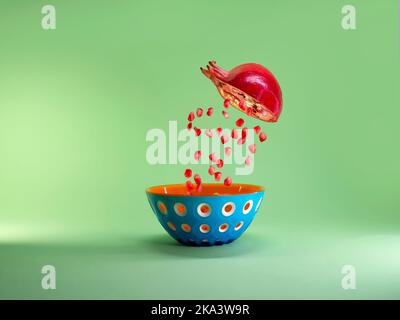 Halbierte Granatapfel mit Granatapfelkernen, die in eine Schüssel fallen, die wie ein Granatapfel aussieht Stockfoto