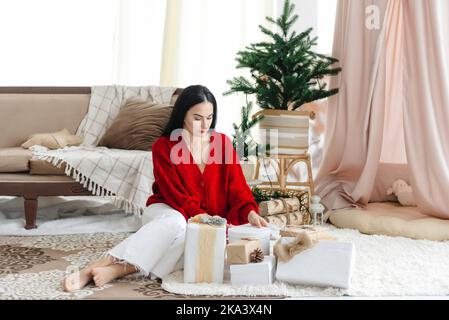 Ein Mädchen öffnet Geschenke. Ein junges Mädchen sitzt zwischen Weihnachts- und Neujahrsgeschenken Stockfoto