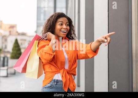Glücklich aufgeregt schockierte junge afroamerikanische Dame in Casual mit einer Menge von Taschen mit Käufen Stockfoto